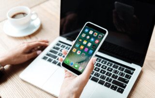 A person sitting at a table using a laptop and smartphone to shop online.
